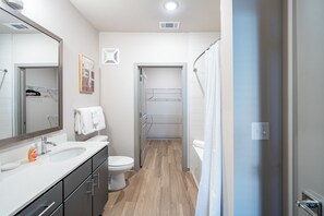 A modern bathroom with a white sink, mirror, and toilet. There is a shower curtain and a towel rack. - Landing Apartments - North Central Pensacola (Pensacola)