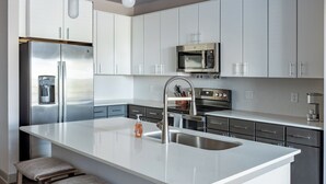 Una cocina moderna con electrodomésticos de acero inoxidable, una isla grande con un lavabo y taburetes de bar.