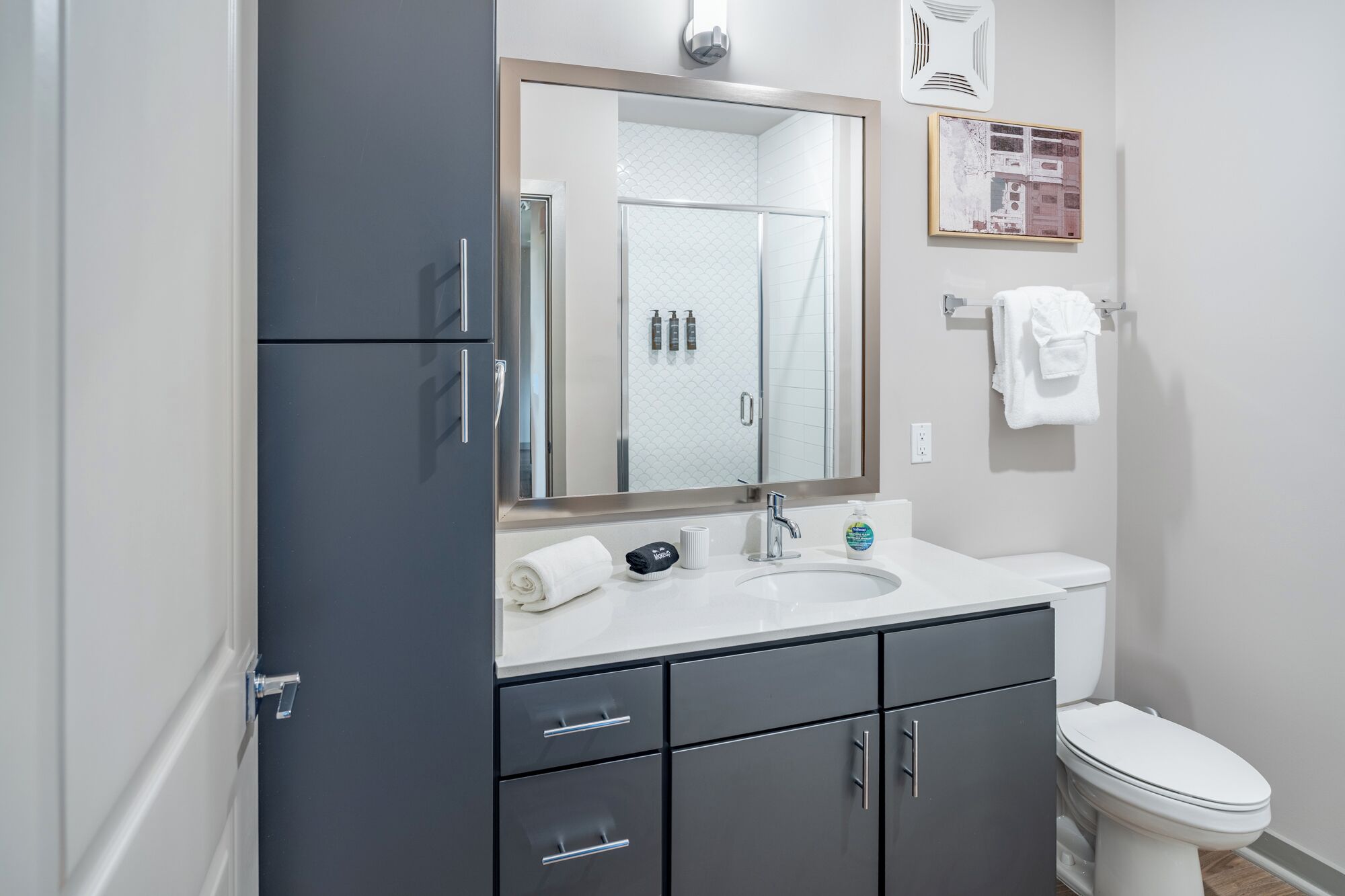 A modern bathroom with a large mirror, a sink, a toilet, and a shower enclosure.