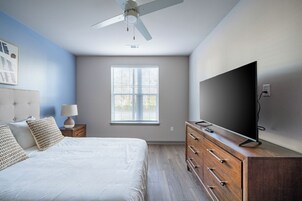 A bedroom with a bed, a dresser, a TV, a ceiling fan, and a window with blinds.
