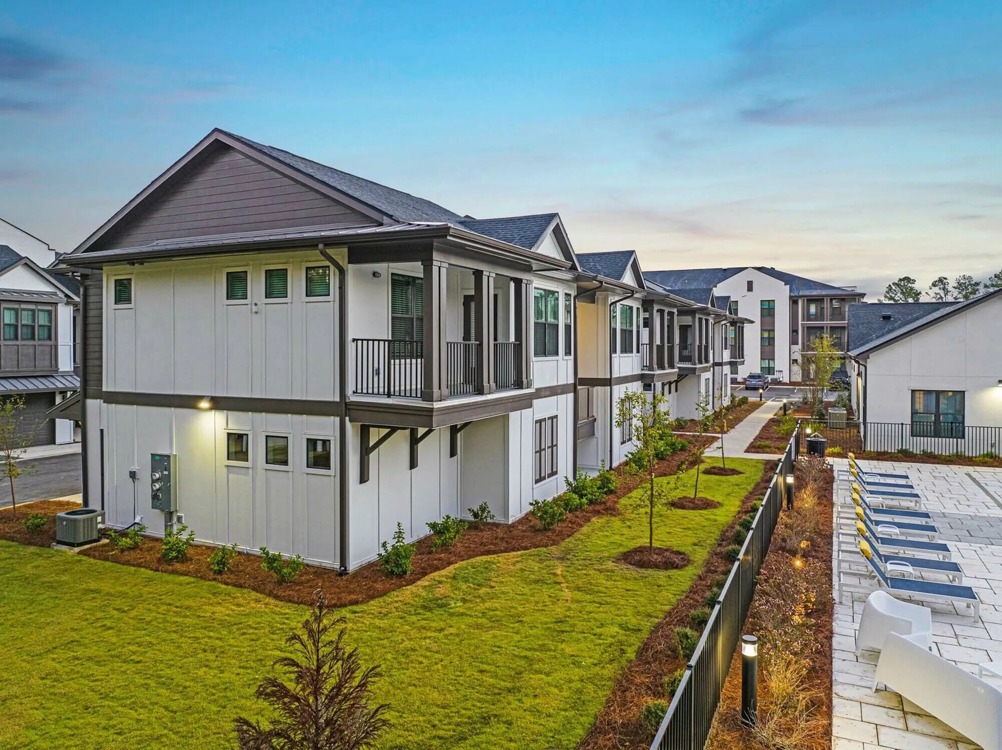 Een rij moderne twee-onder-een-doorwoningen met balkons, een verzorgd gazon en een geplaveid pad.
