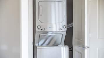 A compact, modern washer and dryer unit in a small laundry room with a door leading to another room.