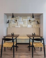 A modern dining area with two black tables, woven chairs, and a patterned wall behind a bench.