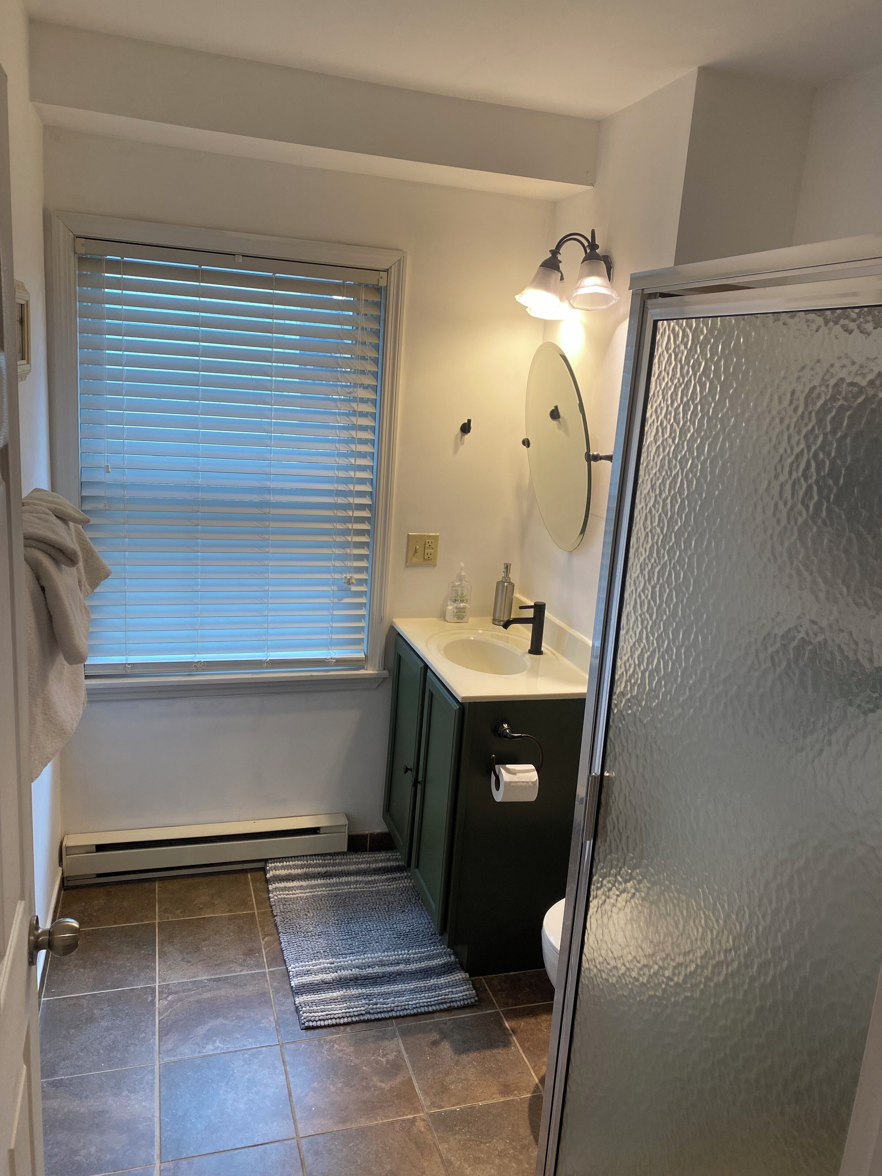 Een badkamer met een raam, een wastafel, een spiegel en een douche.