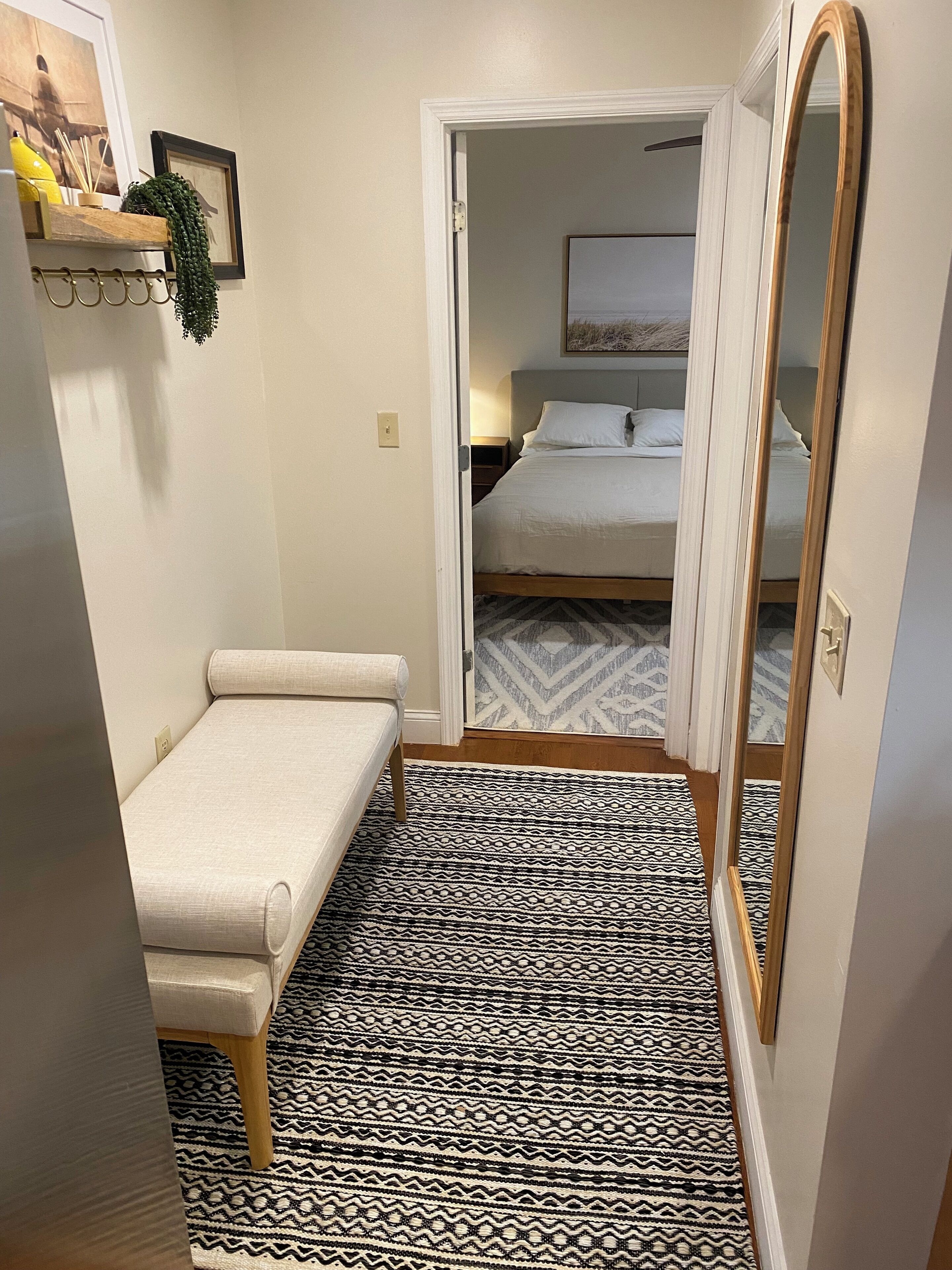 A small, compact room with a single bed, a bedside table, a mirror, and a patterned rug.