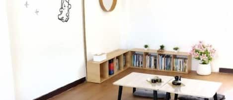 Una habitación acogedora con suelo de madera, una mesita con un cojín, una estantería y una planta en maceta.