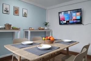 A dining area with a wooden table, chairs, a TV mounted on the wall, and a fruit basket on the table. - Living Room Udonthani (Udon Thani)