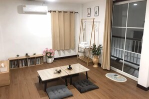 Une pièce avec un plancher en bois, une table avec des coussins, une bibliothèque, une fenêtre avec des rideaux et un balcon avec une balançoire.