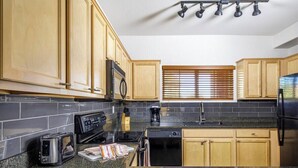A kitchen with granite countertops, wooden cabinets, a black refrigerator, a microwave, a toaster, and a coffee maker.