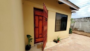 Un bâtiment avec une porte en bois, une fenêtre grillagée et des plantes en pot au sol.