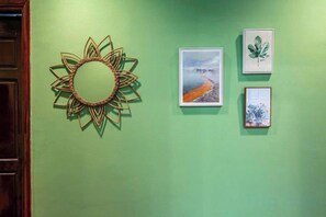 A wall with a decorative sun-like object, a framed landscape painting, and two framed botanical prints.