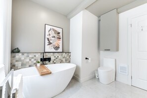 Un baño moderno con una bañera independiente, un salpicadero de azulejos, un inodoro y un espejo grande.