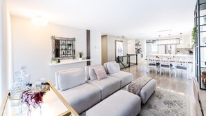 A modern living room with a grey sofa, a coffee table with decorative items, and a dining area with white furniture. - Streamlined apartment with 2 free parking spaces. (Drummondville)
