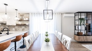 A modern dining area with a long wooden table, white chairs, and a central potted plant. - Streamlined apartment with 2 free parking spaces. (Drummondville)