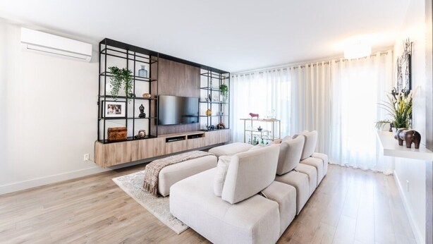 A modern living room with a sectional sofa, a TV mounted on a wooden cabinet, and a decorative shelf with plants. - Streamlined apartment with 2 free parking spaces. (Drummondville)