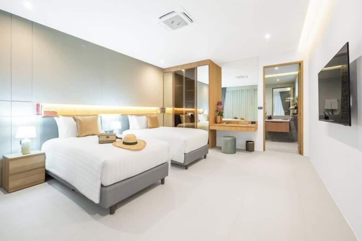 A modern hotel room with two beds, a large mirror, a vanity, and a television.