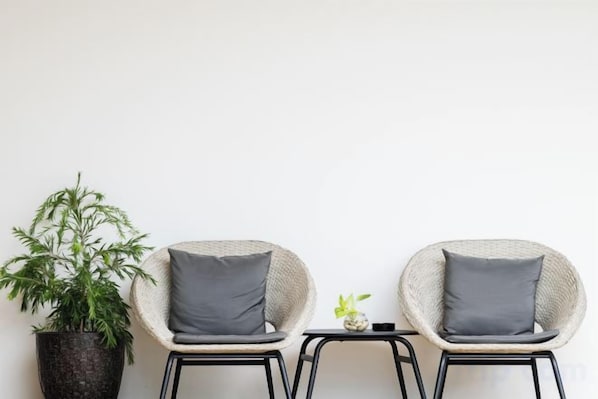 Twee rieten stoelen met grijze kussens, een klein tafeltje met een plant erop, en een bloempot naast de stoelen.