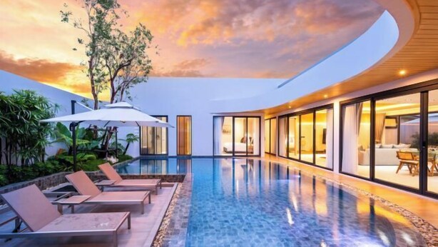 Un área de piscina moderna con sillas de descanso y una sala con paredes de vidrio.
