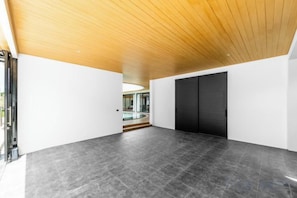 Een ruime binnenruimte met een houten plafond, een zwarte deur en een glazen wand.