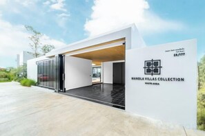 Una villa moderna con entrada de vidrio, una placa con el nombre y cielo despejado.