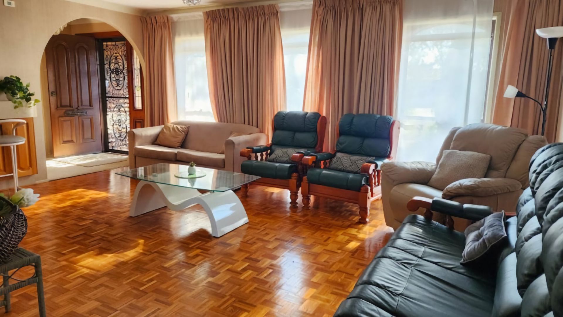 A living room with a sofa, two armchairs, a glass coffee table, and a wooden floor.
