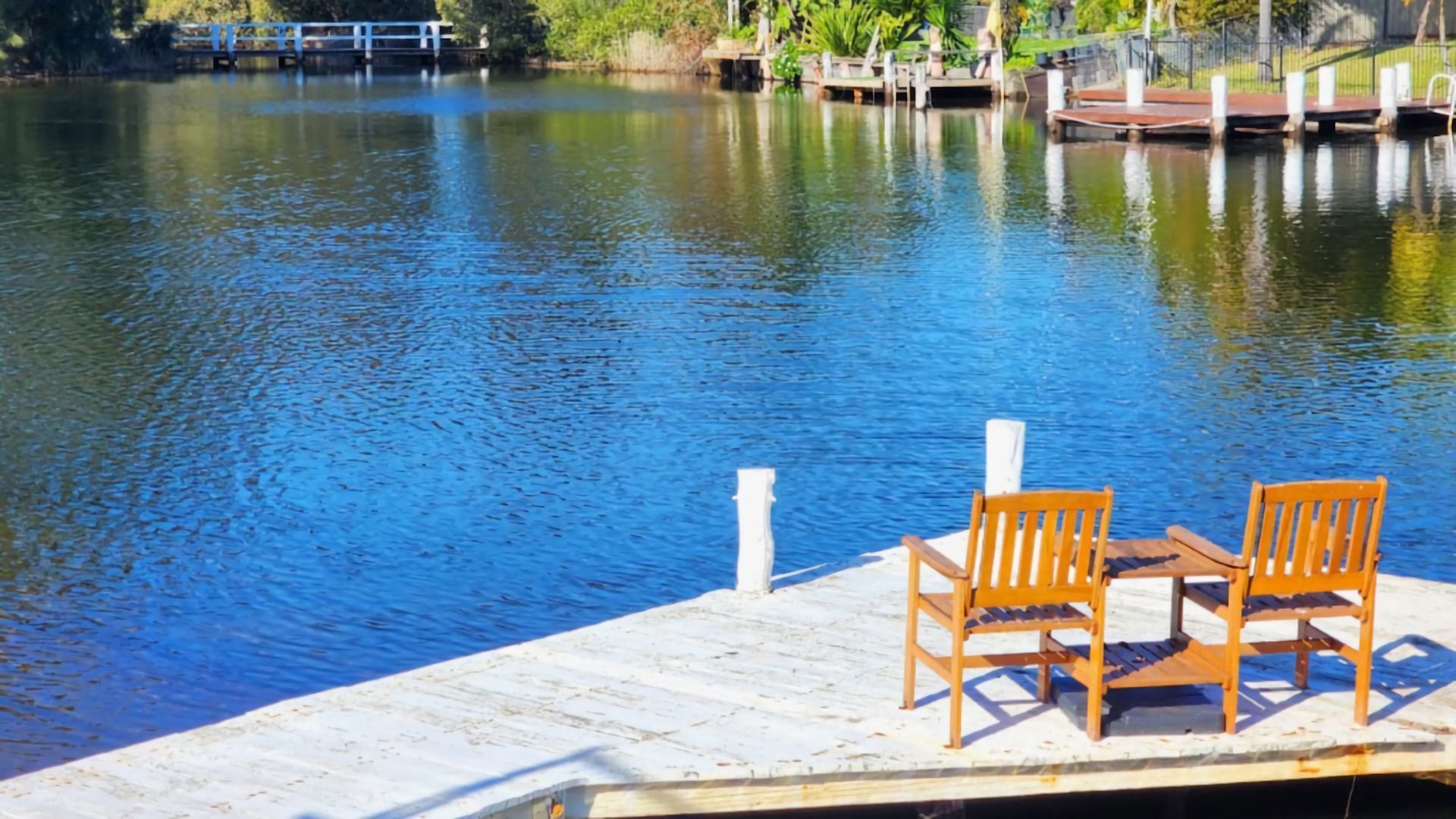 Une jetée en bois avec deux chaises donnant sur une étendue d’eau calme.