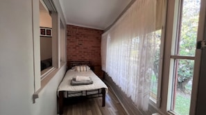 A narrow room with a bed, a brick wall, and a window with curtains.