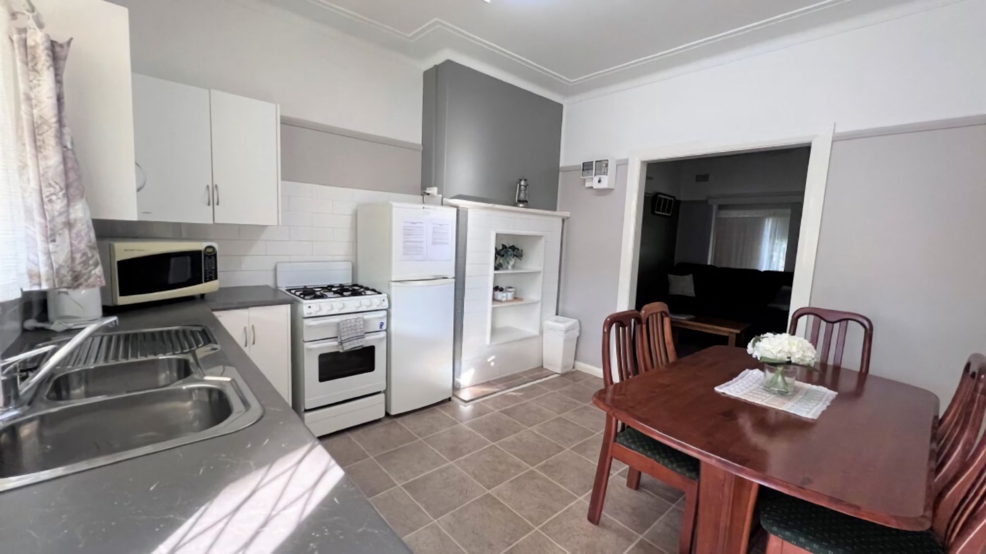 Cocina compacta con estufa, microondas y lavamanos. Cuenta con una mesa de comedor, sillas y un refrigerador pequeño.