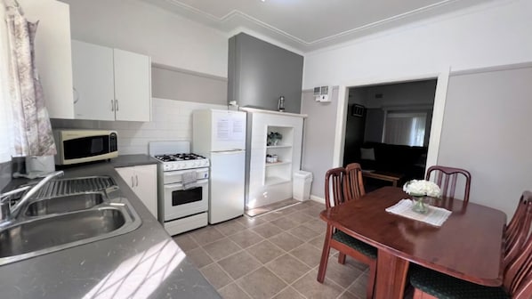 Cocina compacta con estufa, microondas y lavamanos. Cuenta con una mesa de comedor, sillas y un refrigerador pequeño.
