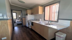 A compact kitchen with wooden cabinets, a stainless steel sink, and a window with curtains.