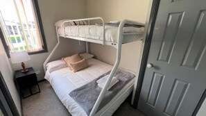 A bunk bed room with a window, a bedside table, and a door. - Cottage 3 ~ Family cottage at Sussex House Holiday Park (Sussex Inlet)