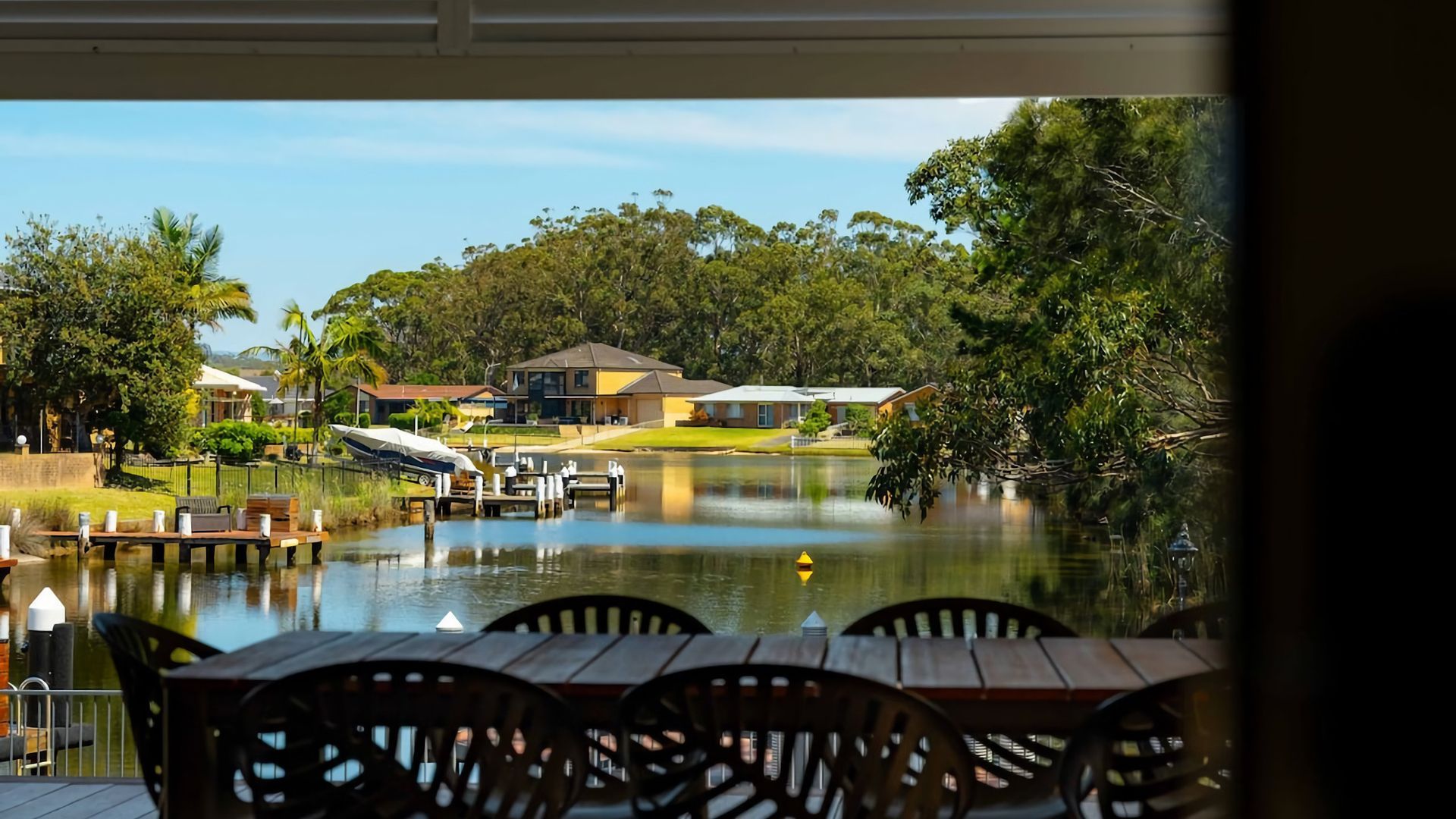 A lakeside view with a dining area, boats, and houses in the background.
