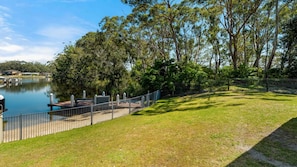 Un parque junto al lago con césped, un muelle y una valla.