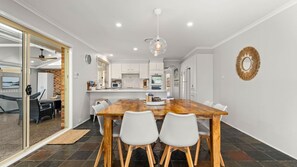Ein moderner Essbereich mit Holztisch und weißen Stühlen, im Hintergrund eine Küche und ein dekorativer Spiegel an der Wand.