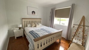Ein Schlafzimmer mit einem hölzernen Bett, einem Nachttisch, einem Fenster mit Vorhängen und einem Wandbild.