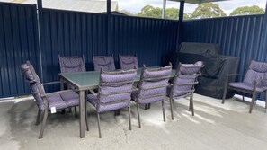 Eine Terrassengruppe mit Tisch und Stühlen, ein überdachter Grill und eine blaue Wand.