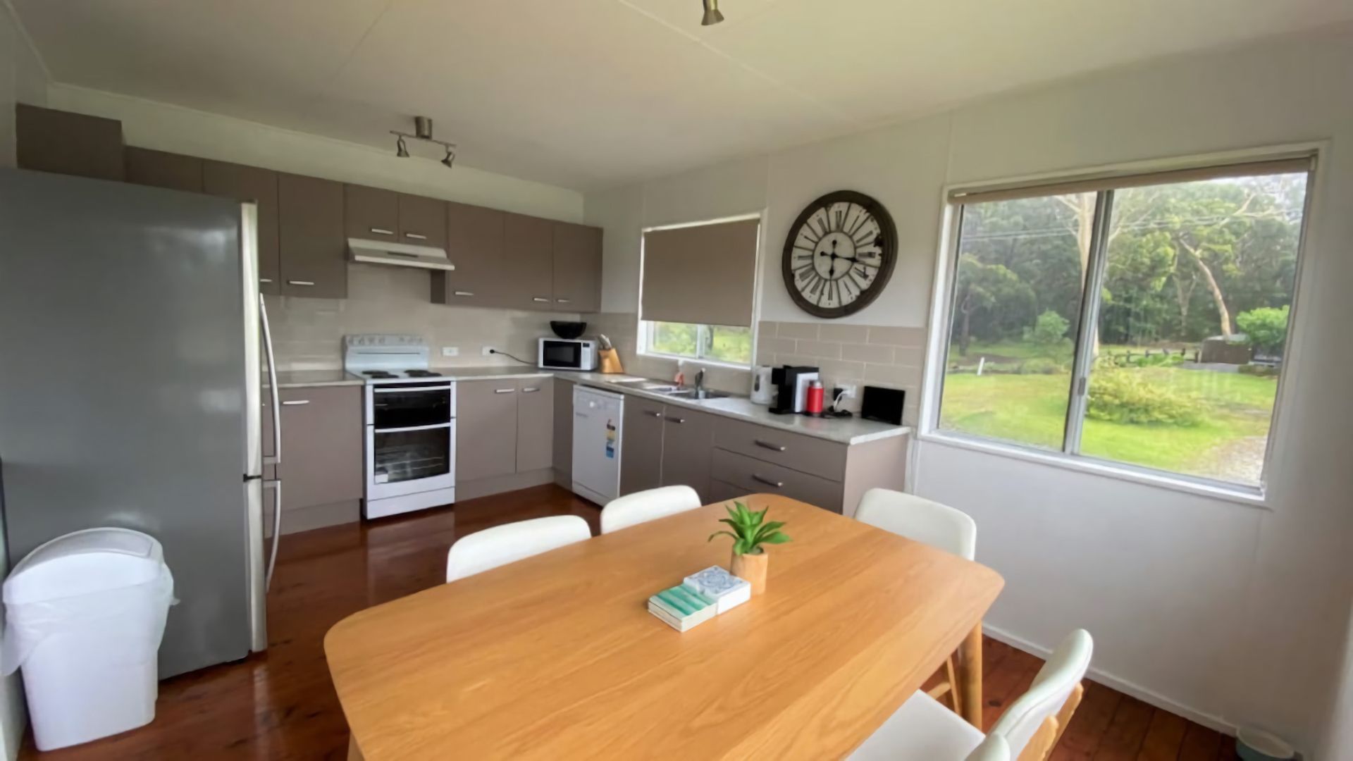 A modern kitchen with a dining area, white cabinetry, and a large window with a view of greenery.