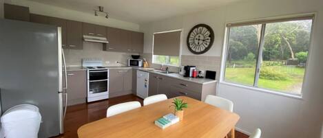 A modern kitchen with a dining area, white cabinetry, and a large window with a view of greenery.