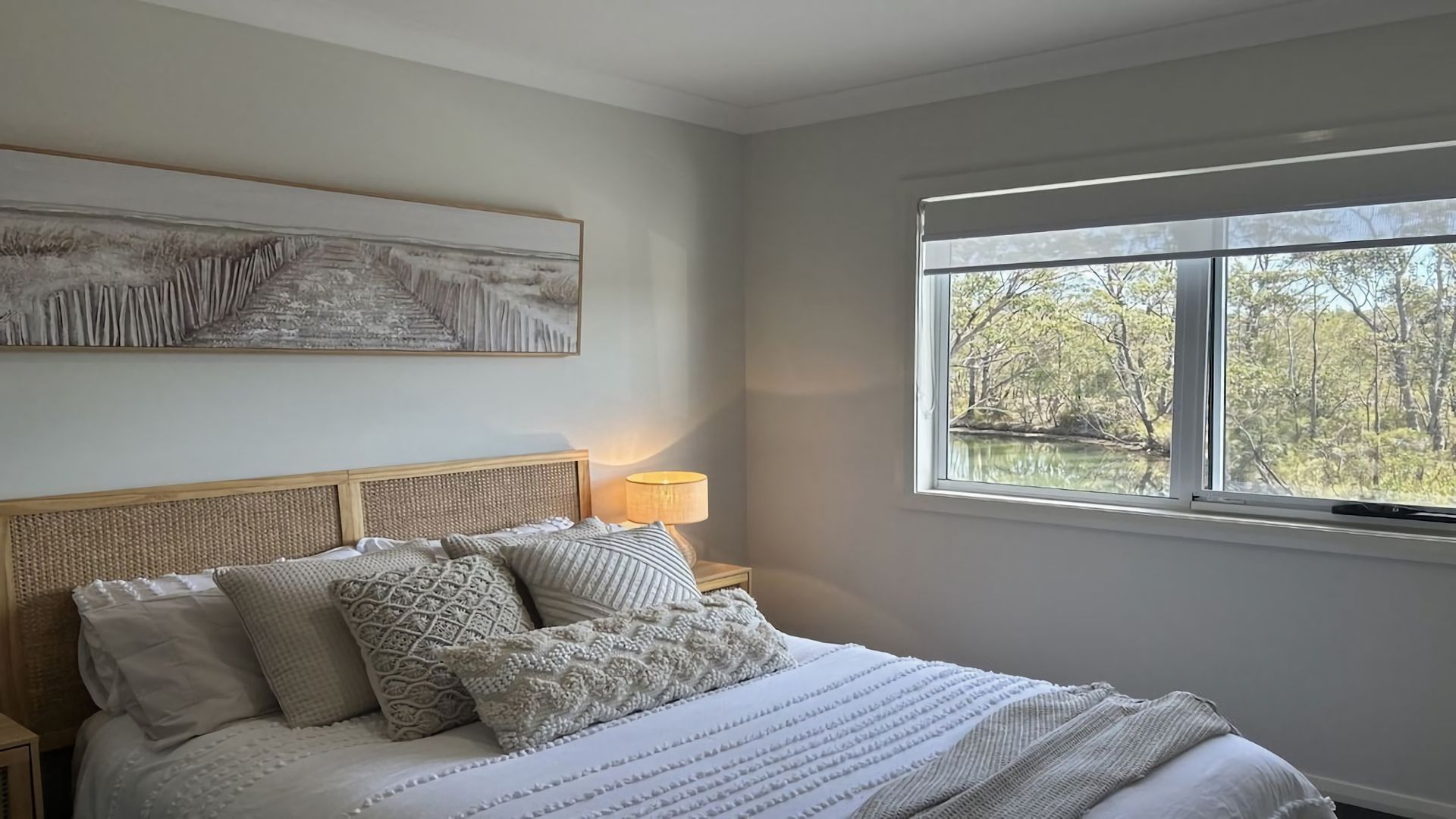 A bedroom with a bed, pillows, a bedside lamp, and a window with a view of trees.