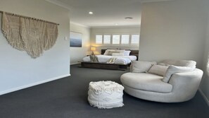 A modern bedroom with a bed, a chair, and a small ottoman. - Sandy Quays on the water (Sussex Inlet)