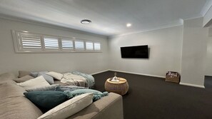 A living room with a sofa, pillows, a round coffee table, a flat-screen TV mounted on the wall, and a window with blinds. - Sandy Quays on the water (Sussex Inlet)