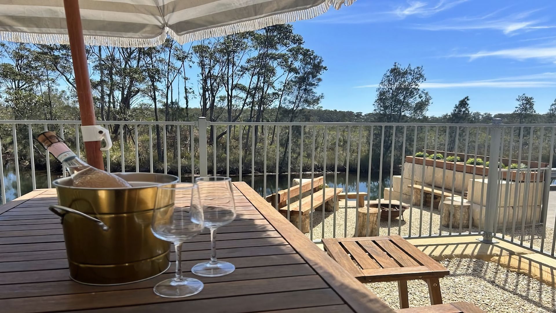 A wooden deck with a table, two wine glasses, and a bottle of champagne.