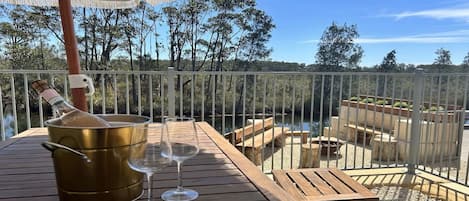 A wooden deck with a table, two wine glasses, and a bottle of champagne.