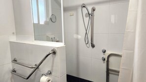 A bathroom with a white tiled wall, a mirror, a shower with a handheld showerhead, and a toilet with a grab bar. - Jopen Motel Unit 1 ~ Stress-free, affordable, and comfortable (Sussex Inlet)
