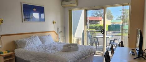 A hotel room with a bed, a desk, a chair, a painting on the wall, and a sliding glass door leading to an outdoor area.
