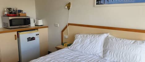 Una camera d'albergo con un letto, un forno a microonde, un frigorifero e un comodino.