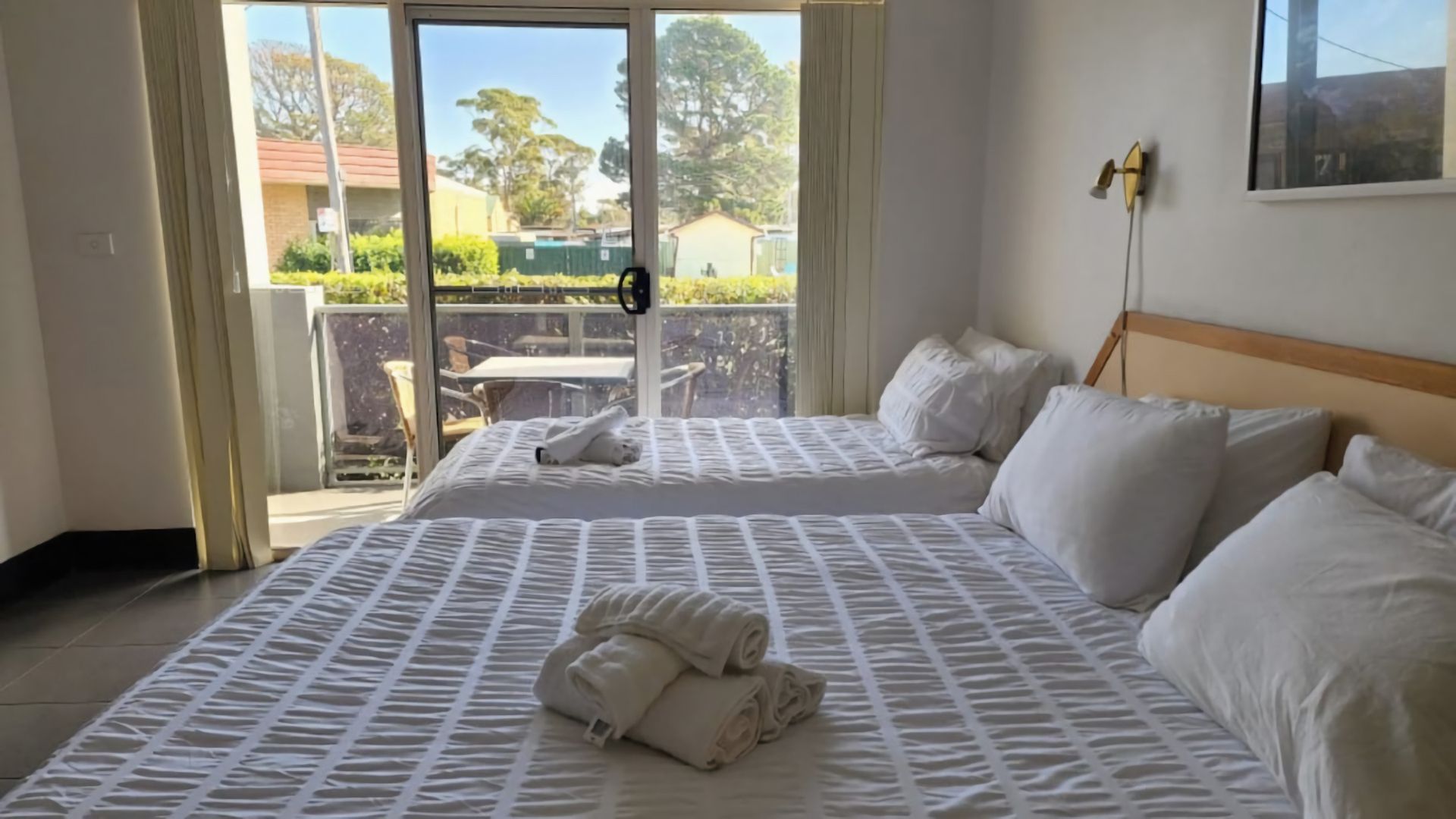 A hotel room with a bed, pillows, a view of the outside, and a balcony.