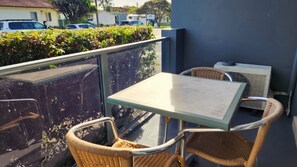 A balcony with wicker chairs and a table, overlooking a street with parked cars and greenery. - Jopen Motel Unit 2 ~ Stress-free, affordable, and comfortable (Sussex Inlet)