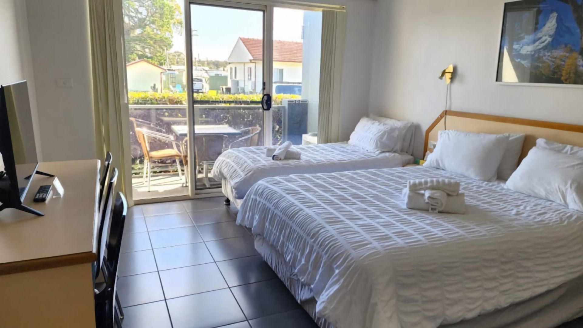 Een hotelkamer met twee bedden, een bureau en uitzicht op buiten.