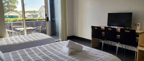 Habitación de hotel con dos camas, un escritorio con silla, televisor y vista al exterior.